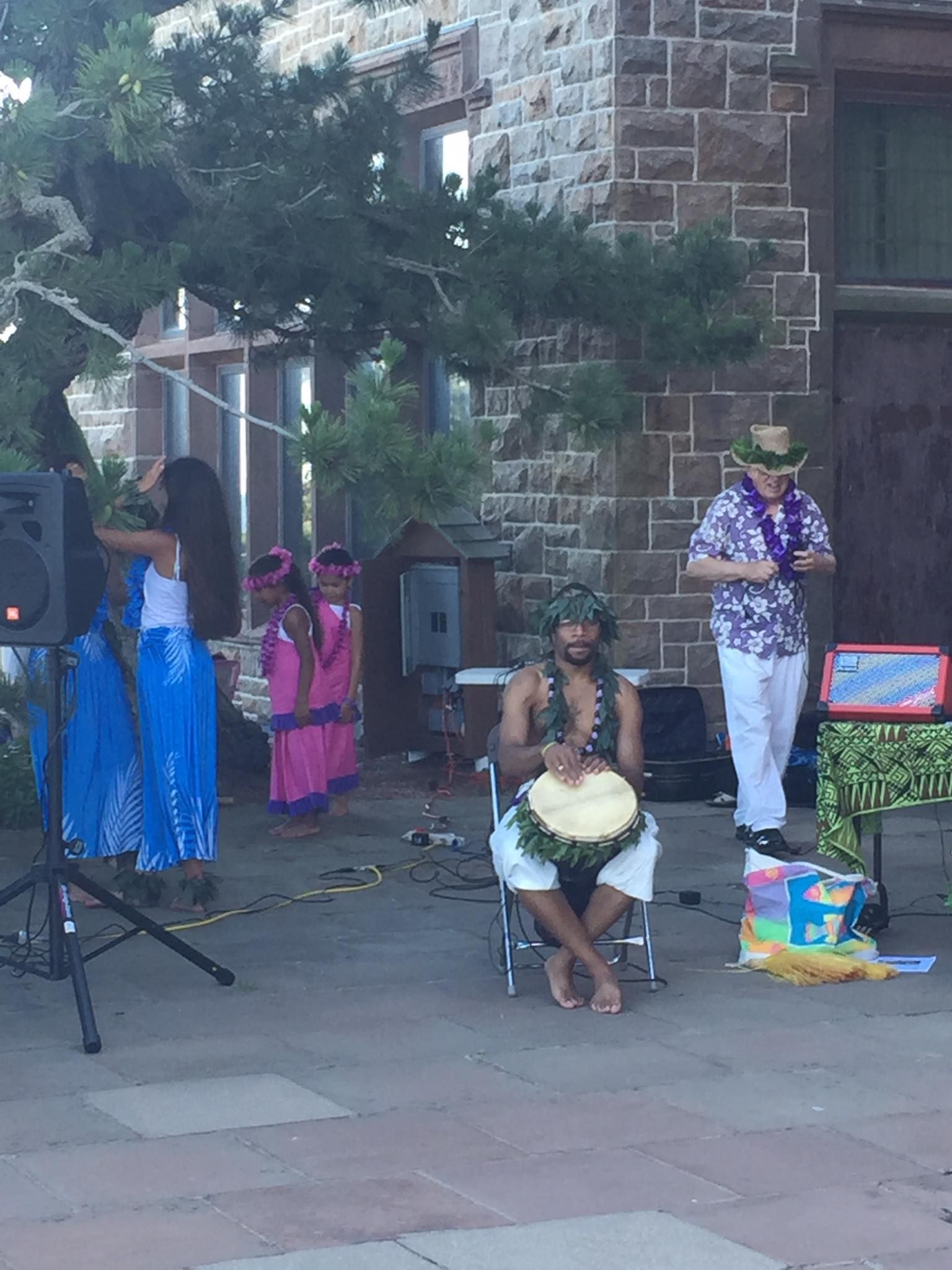 A man is sitting in a chair playing a drum in front of a group of people.
