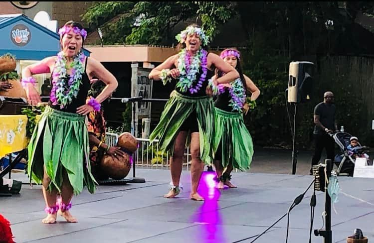 A group of women are dancing hula on a stage.