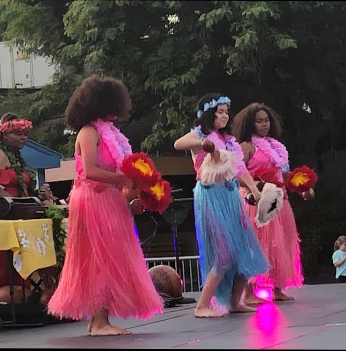 A group of girls in pink and blue dresses are dancing on a stage