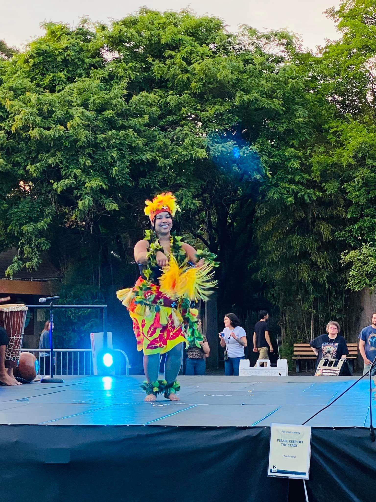A hula dancer is standing on a stage in front of a crowd.