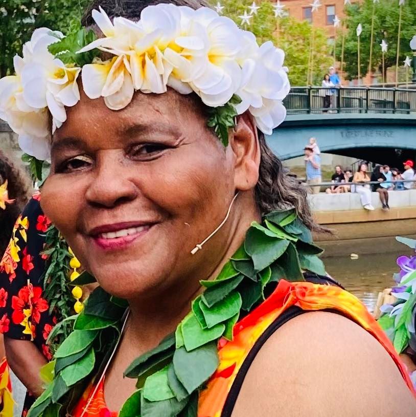 A woman wearing a lei and a flower crown smiles for the camera