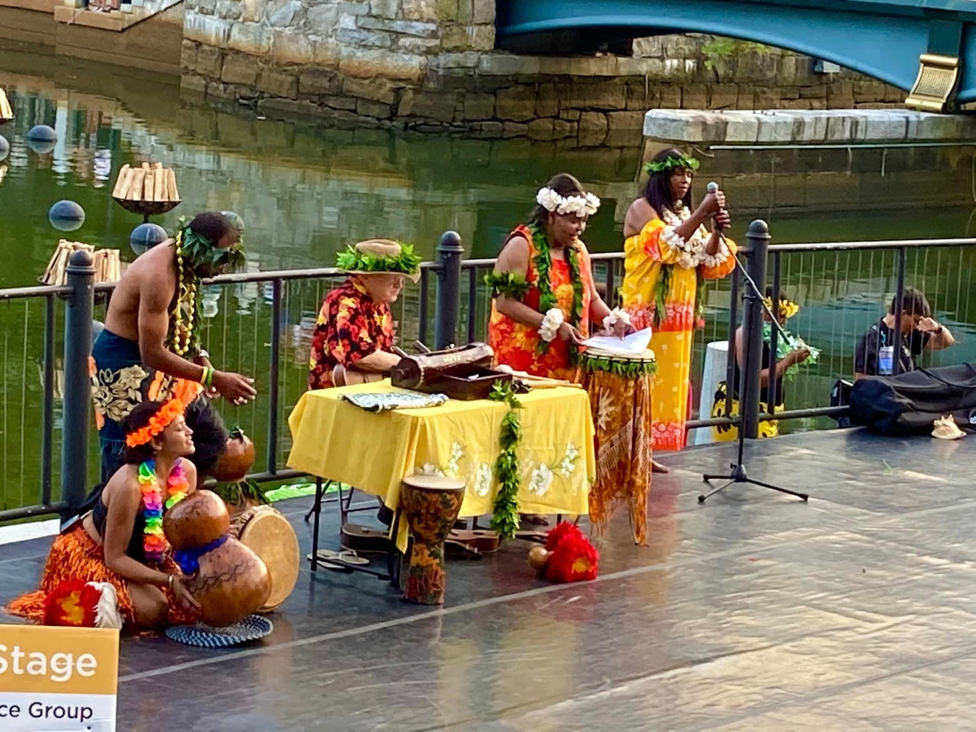 A group of people are playing instruments on a stage in front of a body of water.