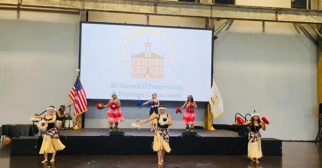 A group of women are dancing on a stage in front of a large screen.