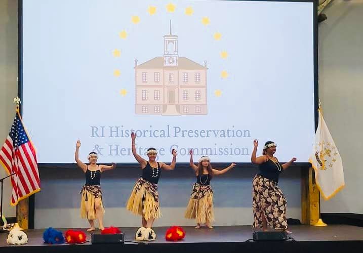 A group of women are dancing on a stage in front of a large screen.