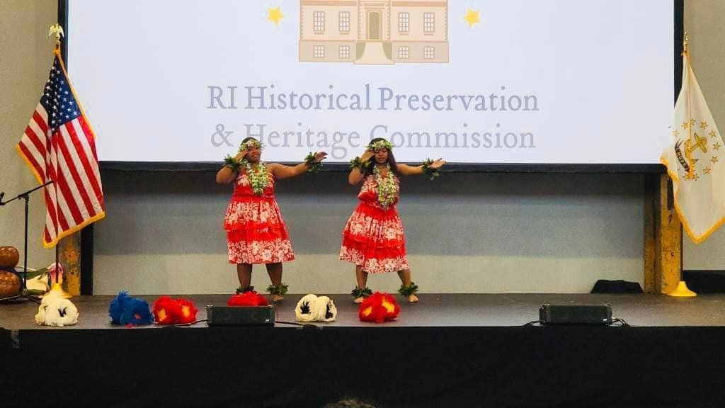 Two women are dancing on a stage in front of a large screen.