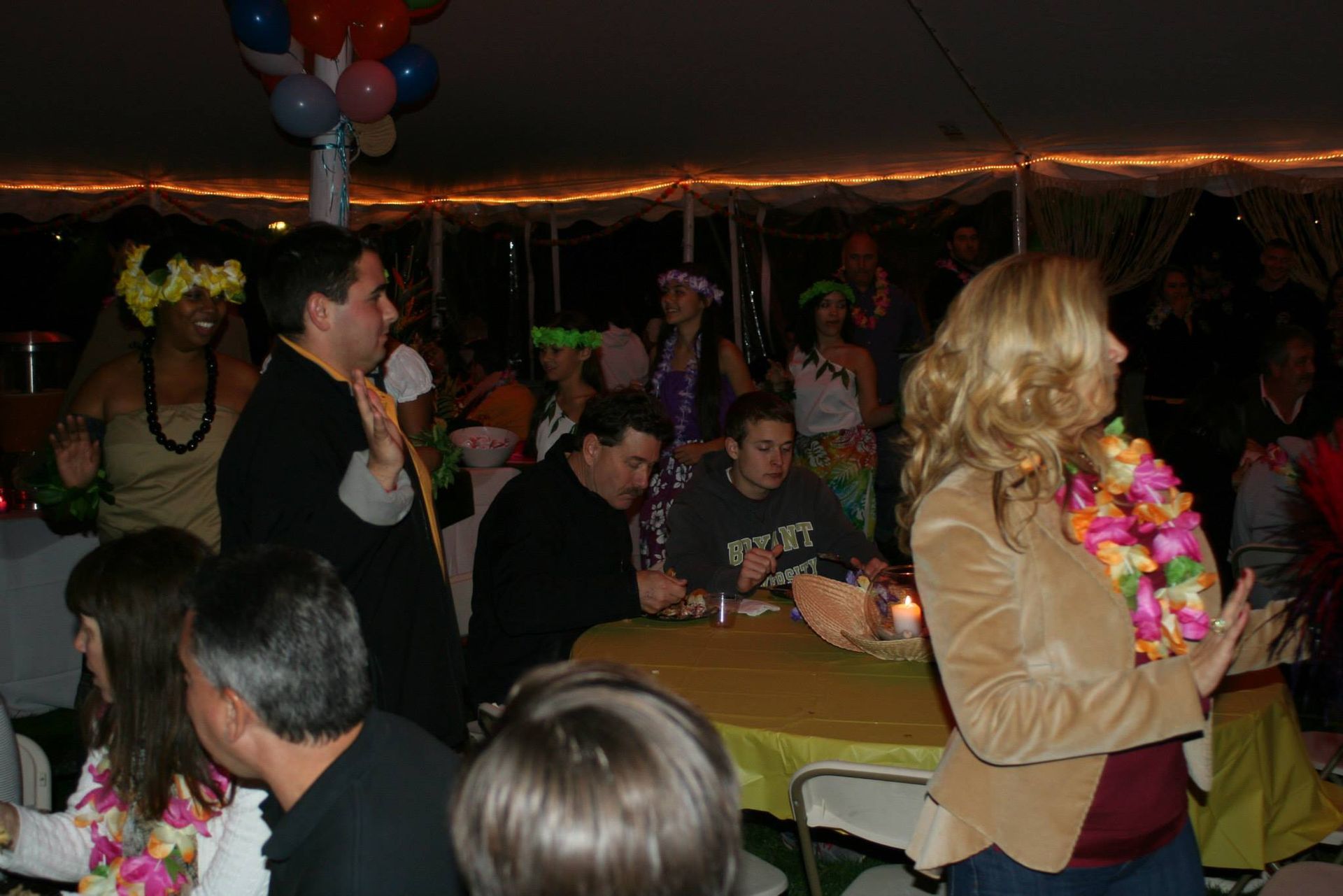 A woman wearing a lei is standing in a crowd of people at a party.