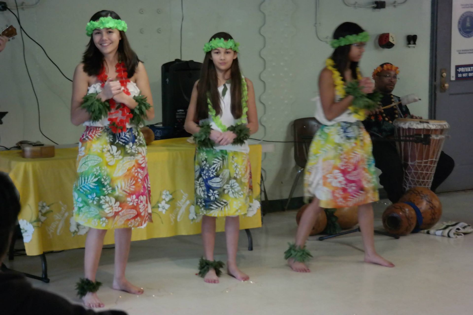 A group of young girls are dancing hula in a room.