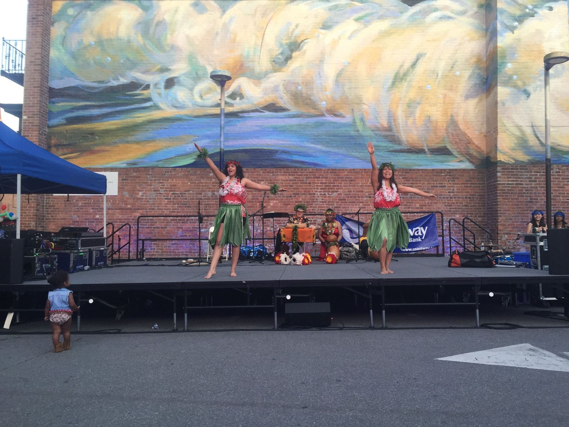 A group of women are dancing on a stage in front of a mural