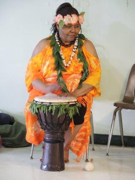 A woman wearing a lei is playing a drum