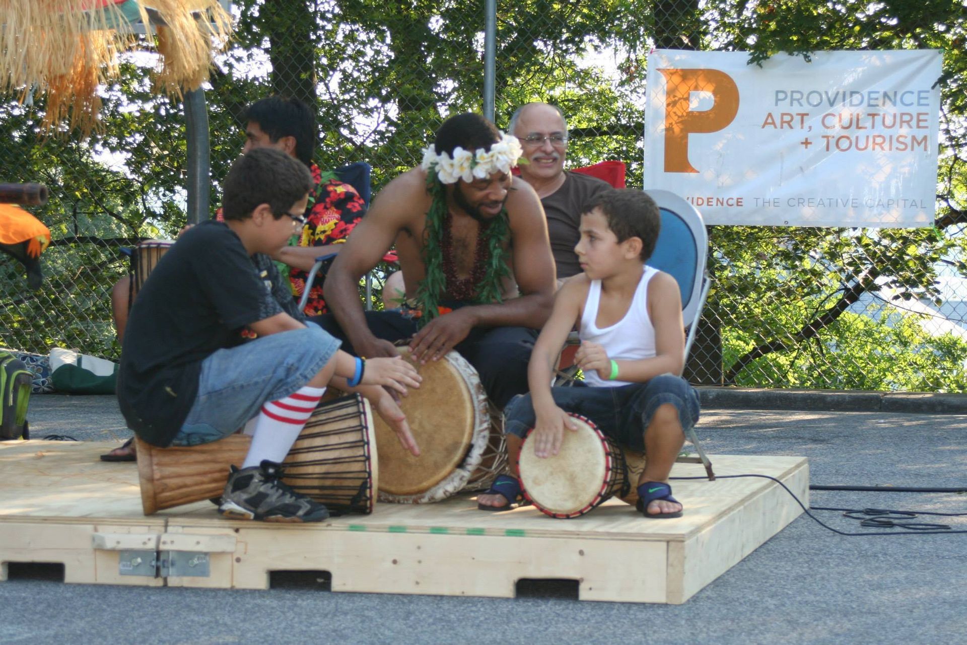 A group of people playing drums in front of a sign that says provides art culture and tourism