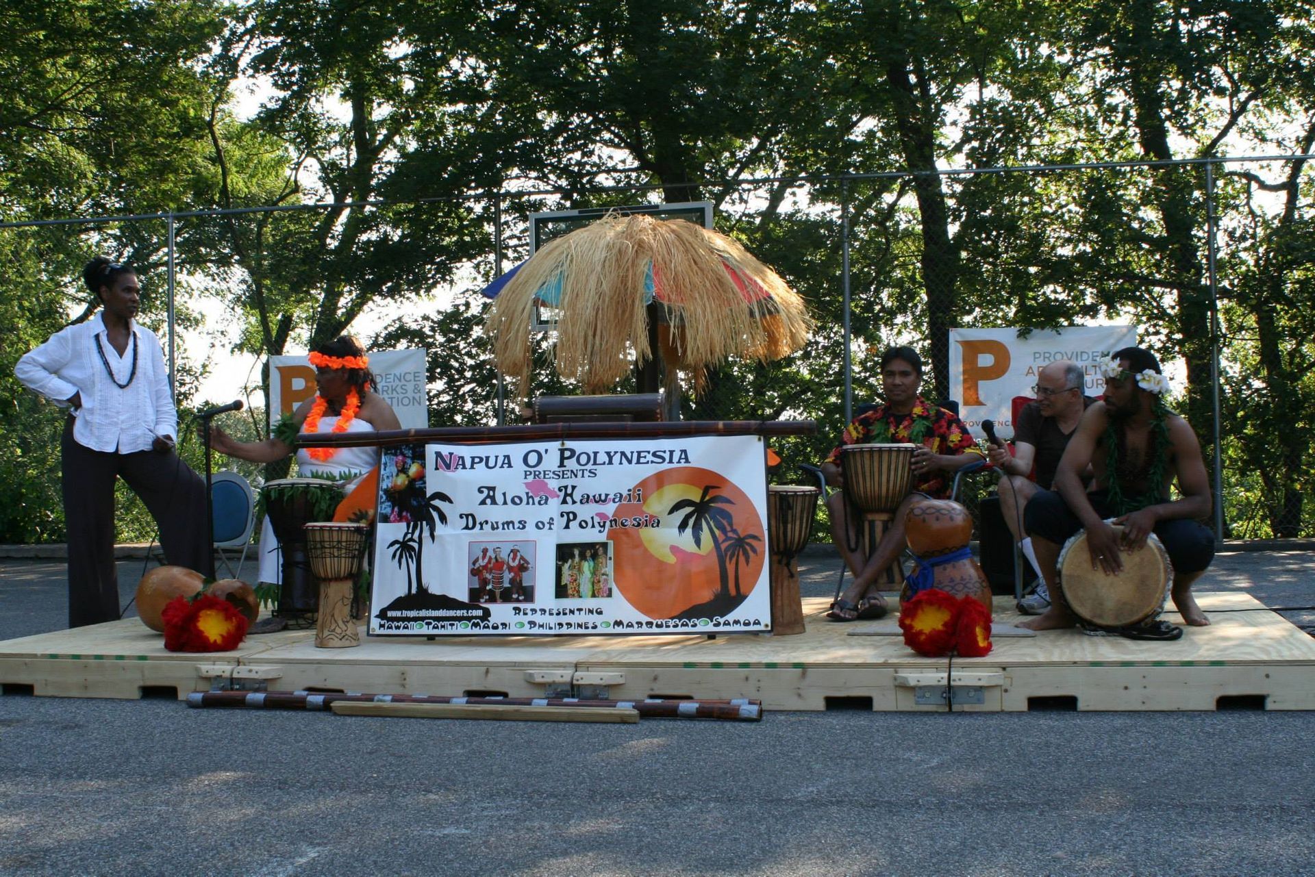 A group of men are playing drums in front of a sign that says ' hawaii ' on it