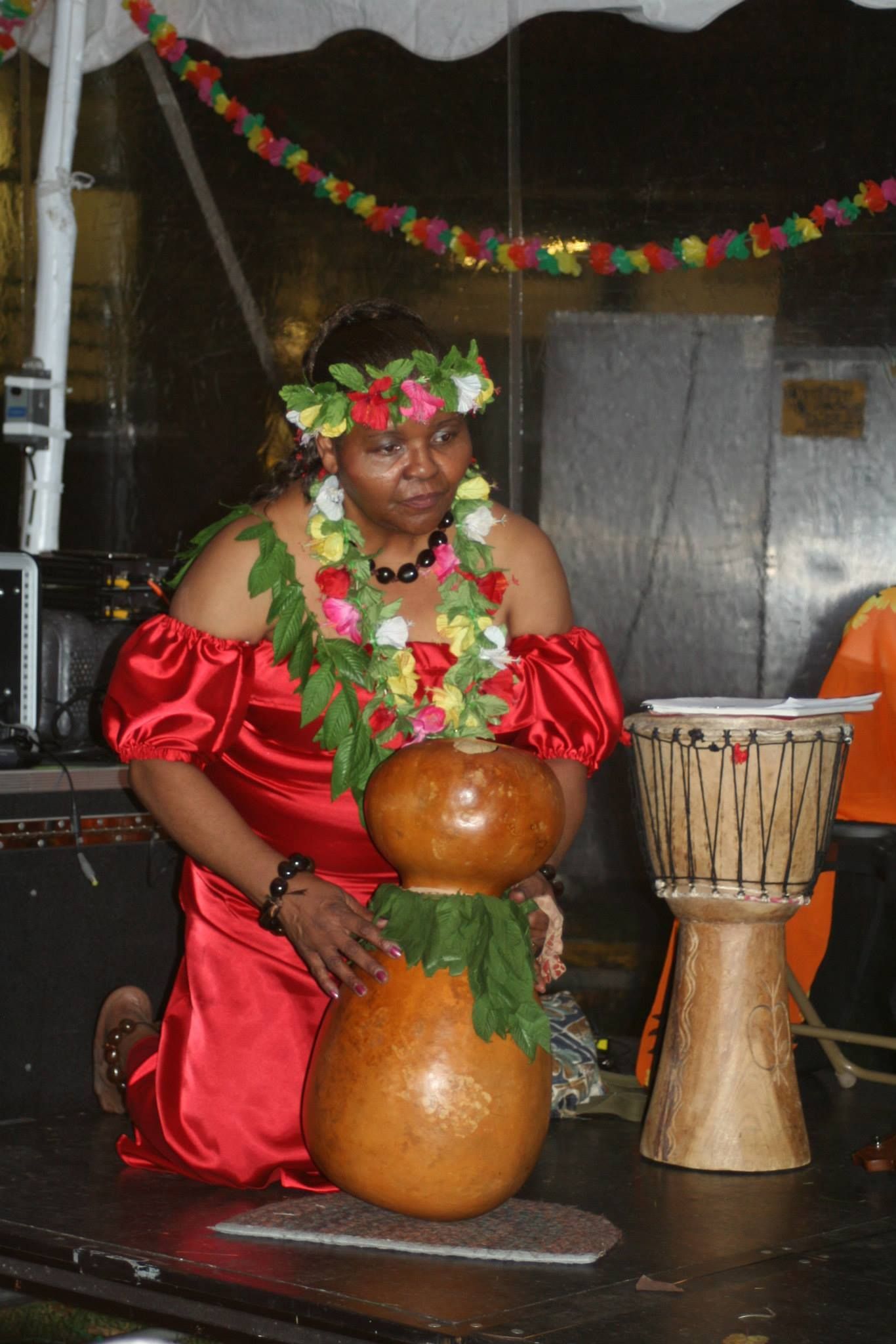 A woman in a red dress is kneeling next to a gourd and a drum
