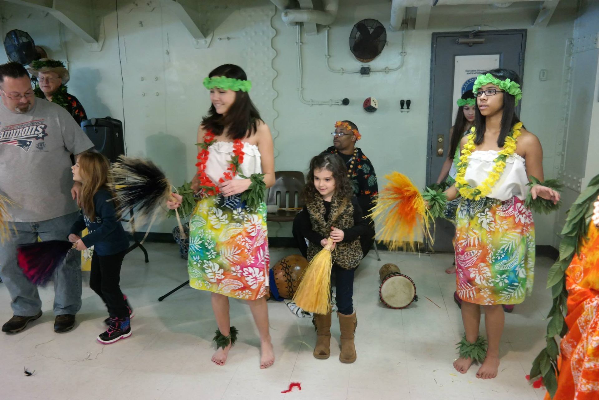 A group of people are dancing hula in a room.