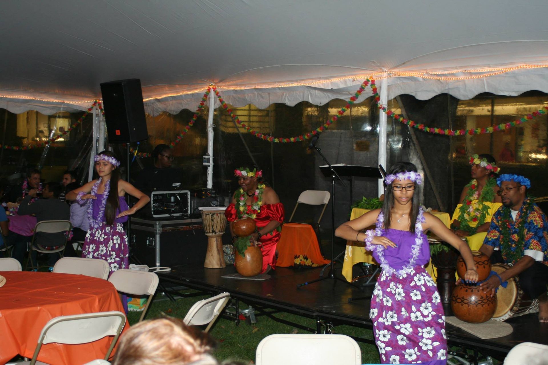 A group of people are performing a hula dance under a tent.
