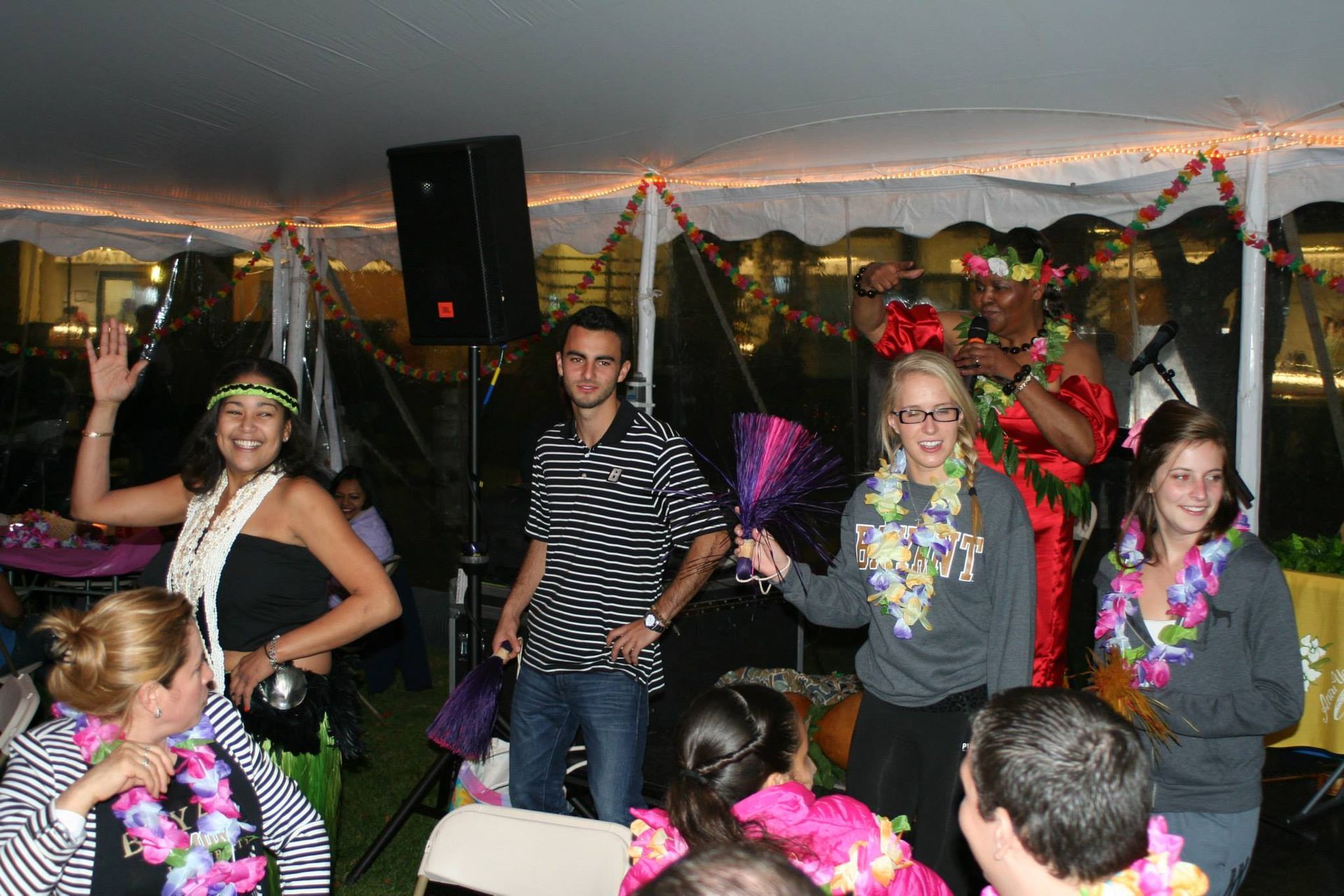 A group of people are dancing under a tent at a party.