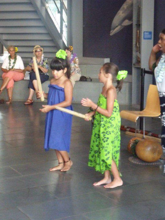 Two little girls in blue and green dresses are holding sticks