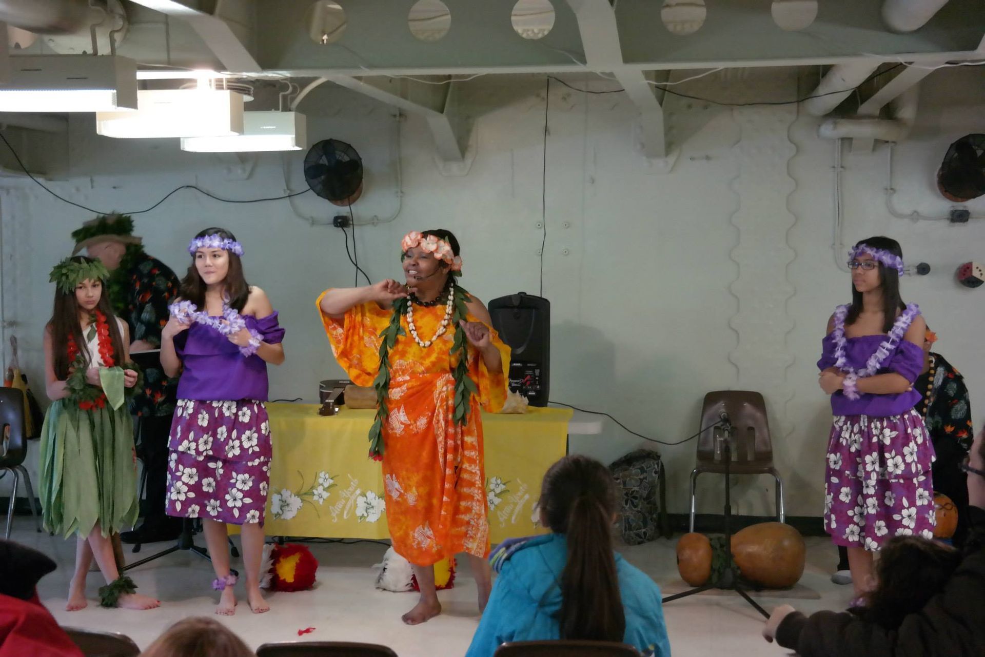 A group of people are performing a hula dance in a room