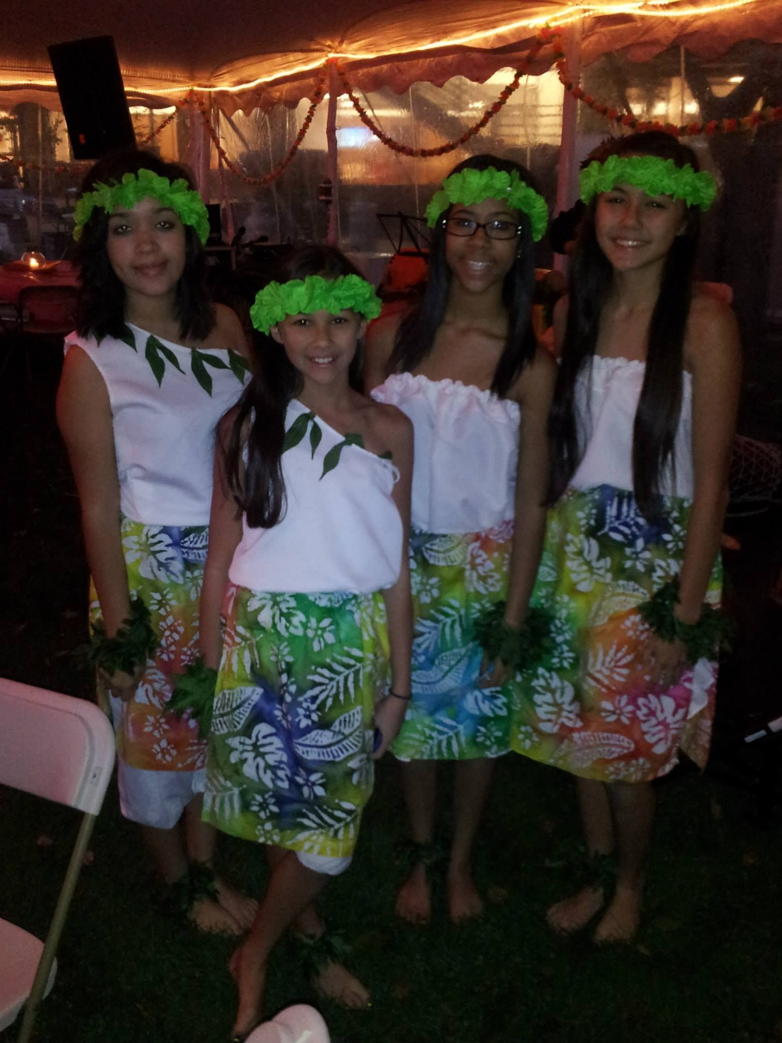 A group of young girls wearing hawaiian outfits are posing for a picture