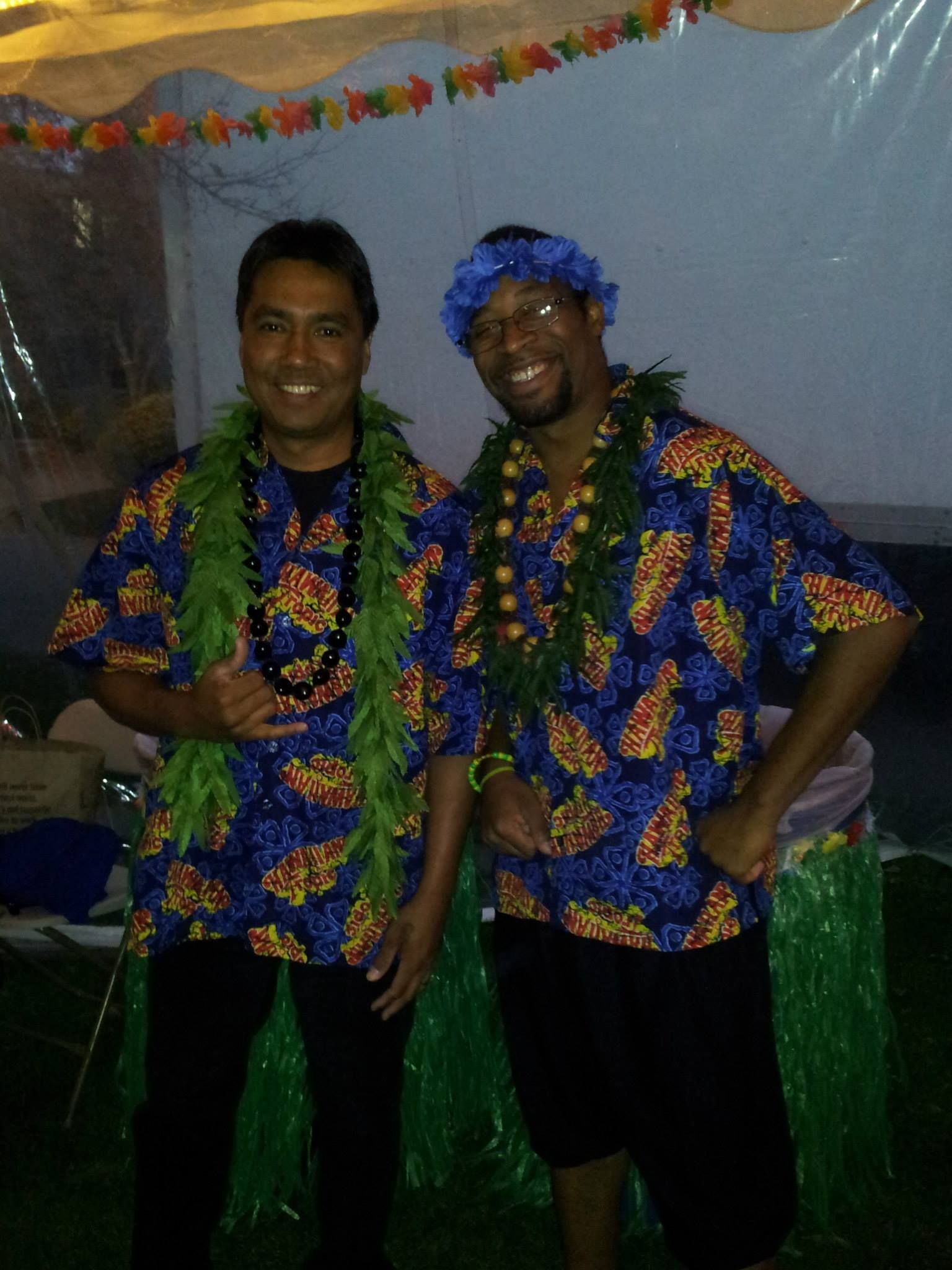 Two men wearing hawaiian shirts and lei are posing for a picture