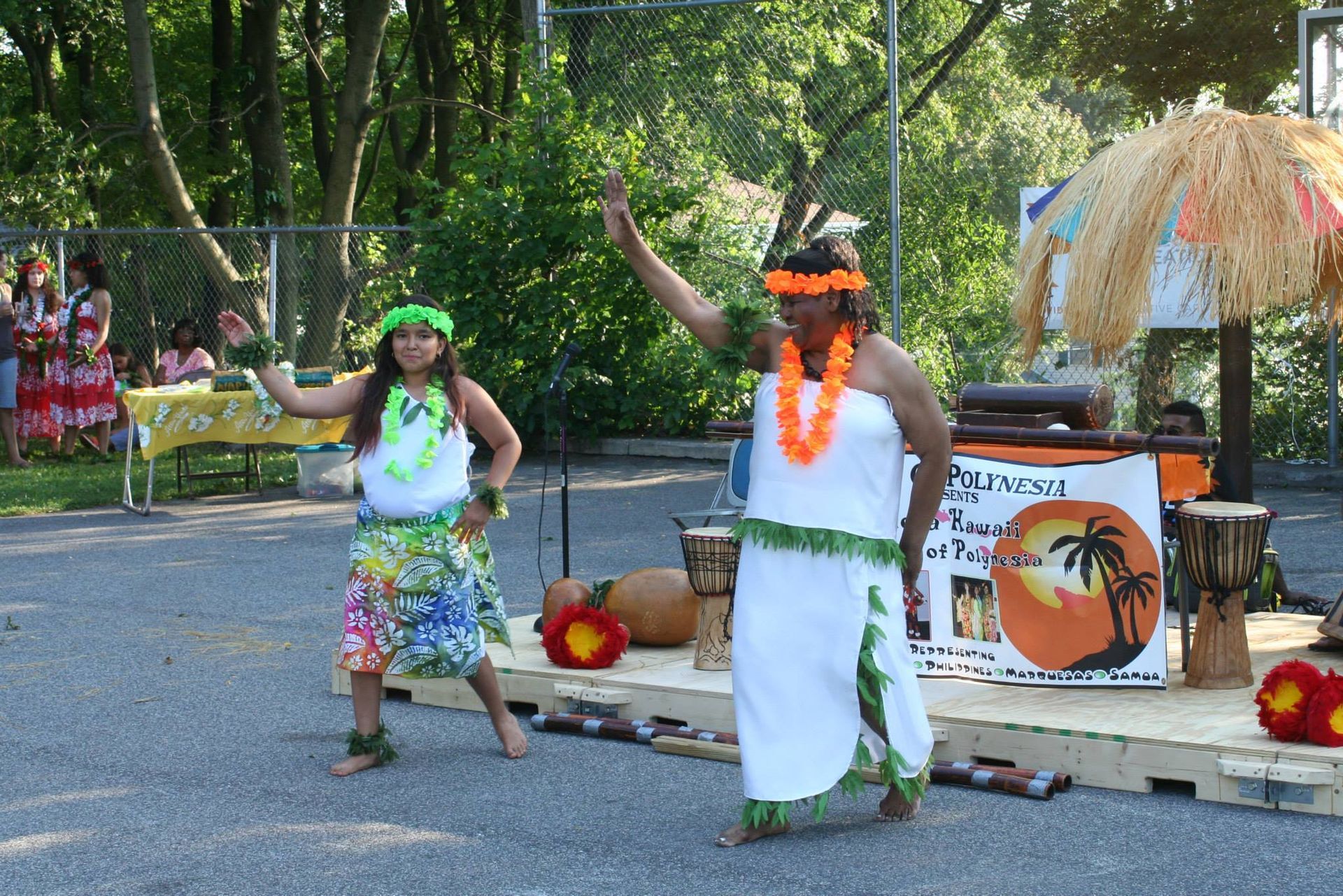 Two women are dancing in front of a sign that says hawaiian