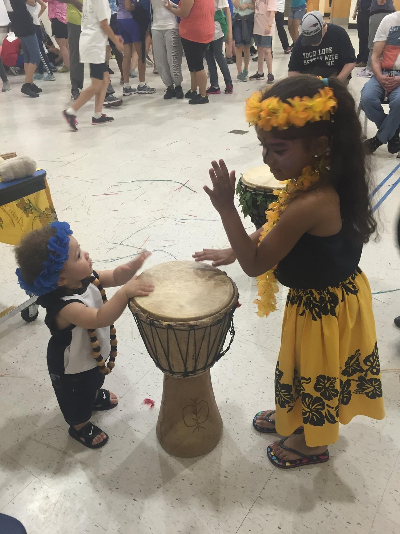 A baby and a girl are playing drums in a room.