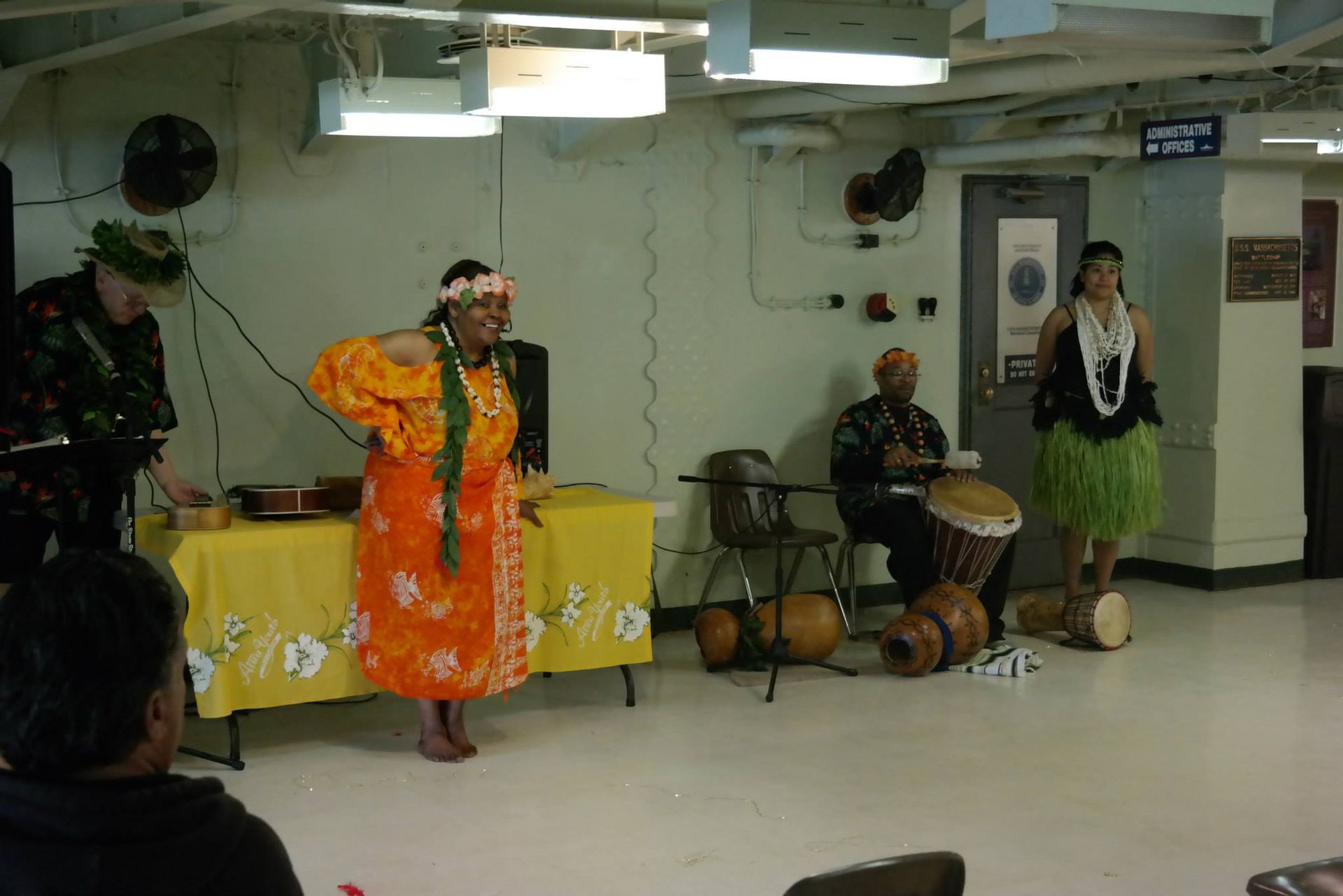 A group of people are performing a hula dance in a room.