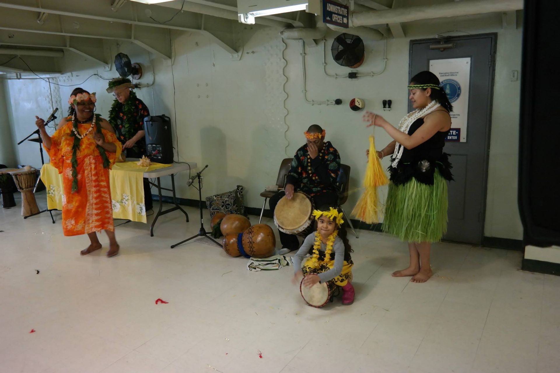 A group of people are performing a hula dance in a room.