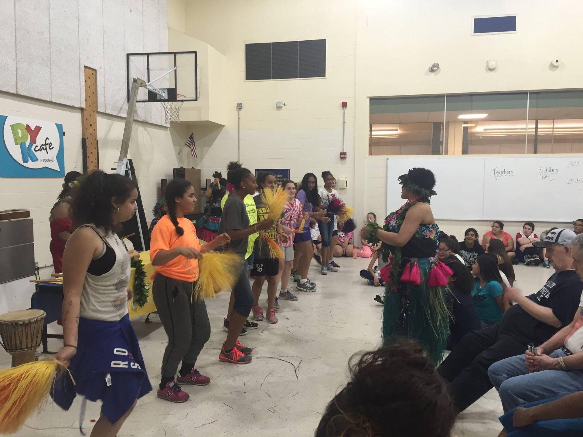 A group of people are dancing in a room with a basketball hoop in the background.