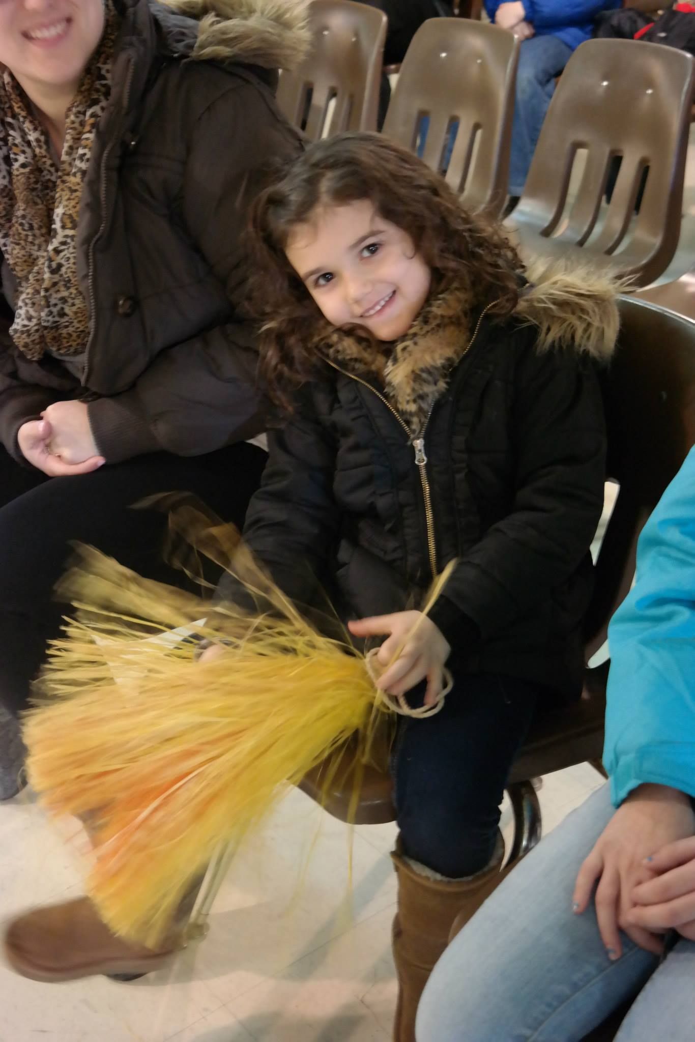 A little girl in a black jacket is holding a yellow fan