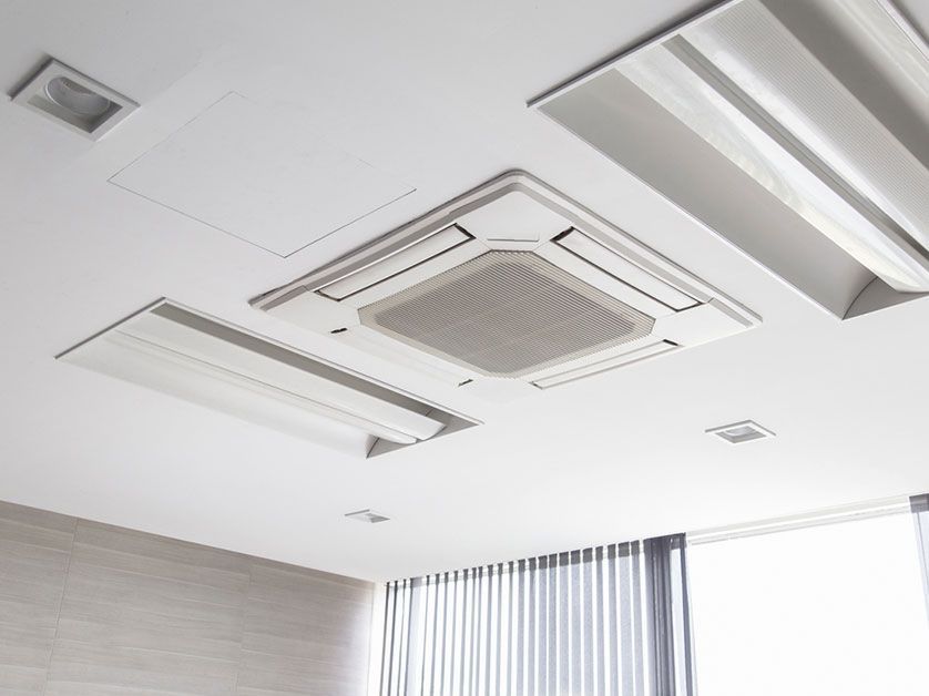 Two air conditioning units on concrete pads next to a red brick building and green grass.