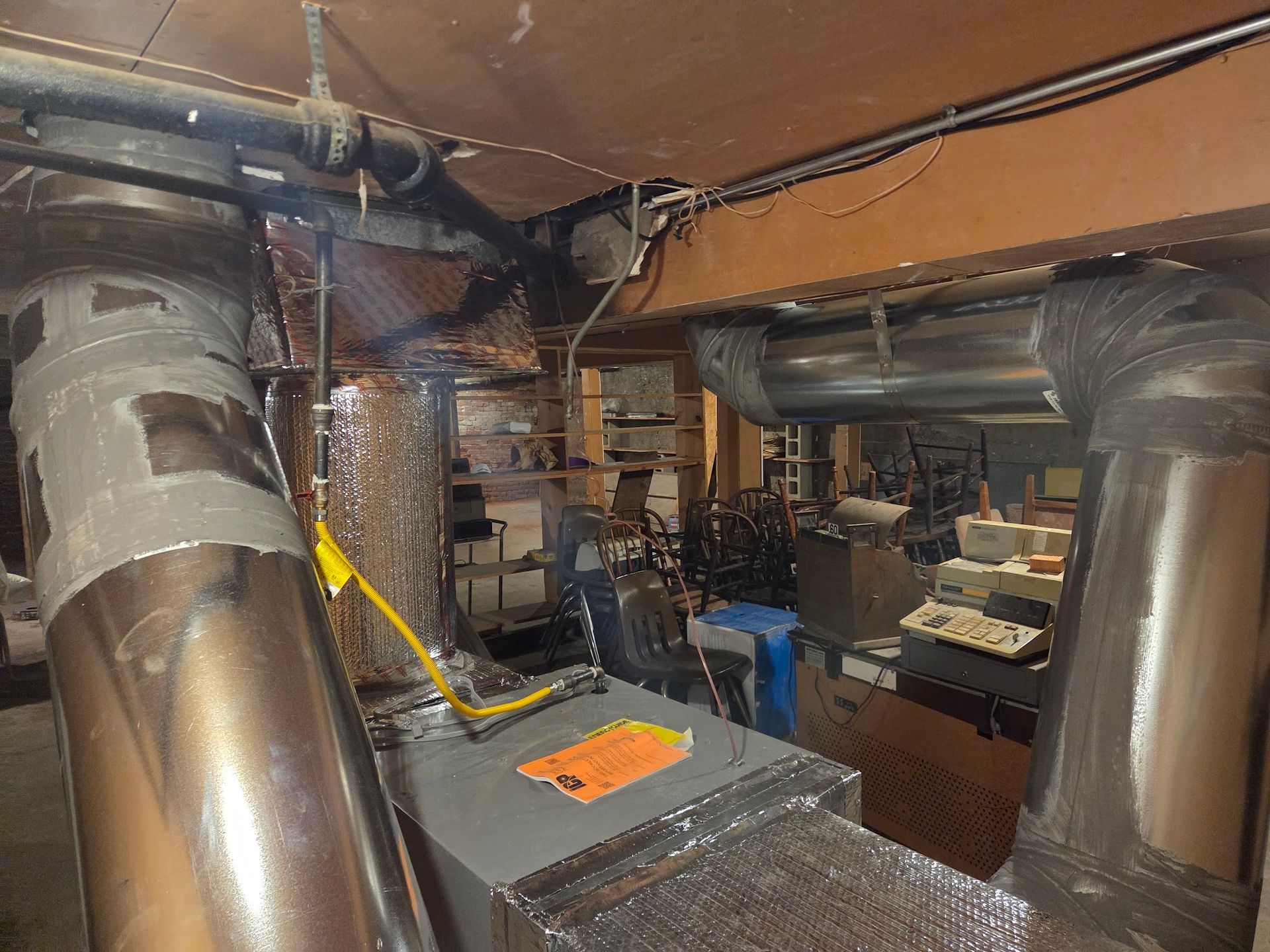 Ductwork and a furnace in a basement. Silver metal ducts and a gray furnace are surrounded by insulation and wires.