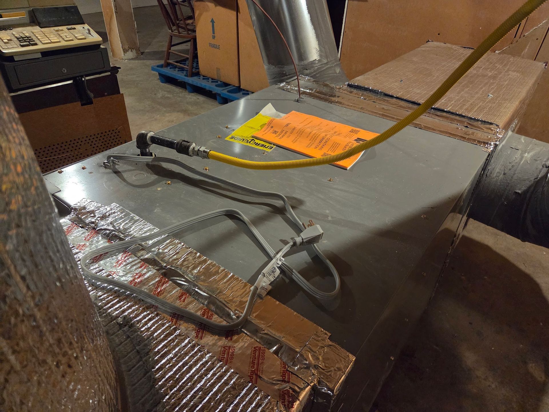 HVAC unit in a basement, with silver ductwork, yellow wiring, and orange note.