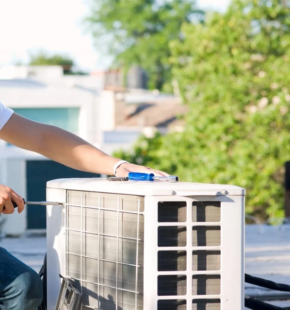 Person repairing an air conditioner unit on a rooftop using a screwdriver.
