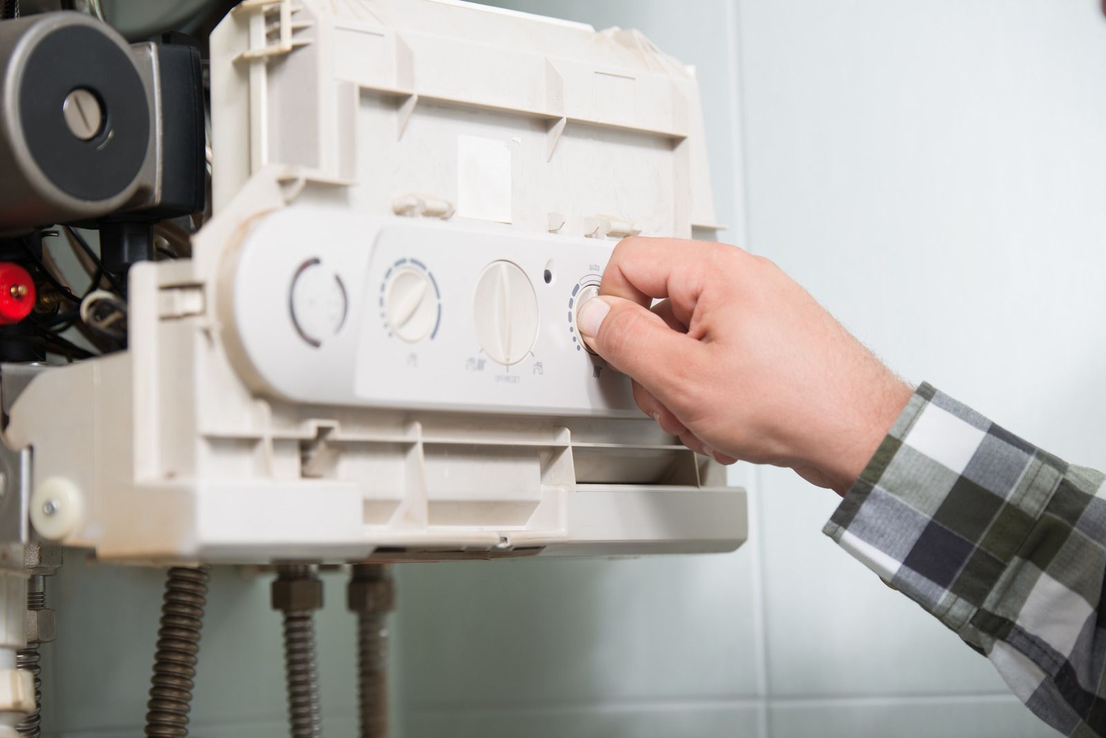 Person adjusting a dial on a white boiler mounted on a wall.