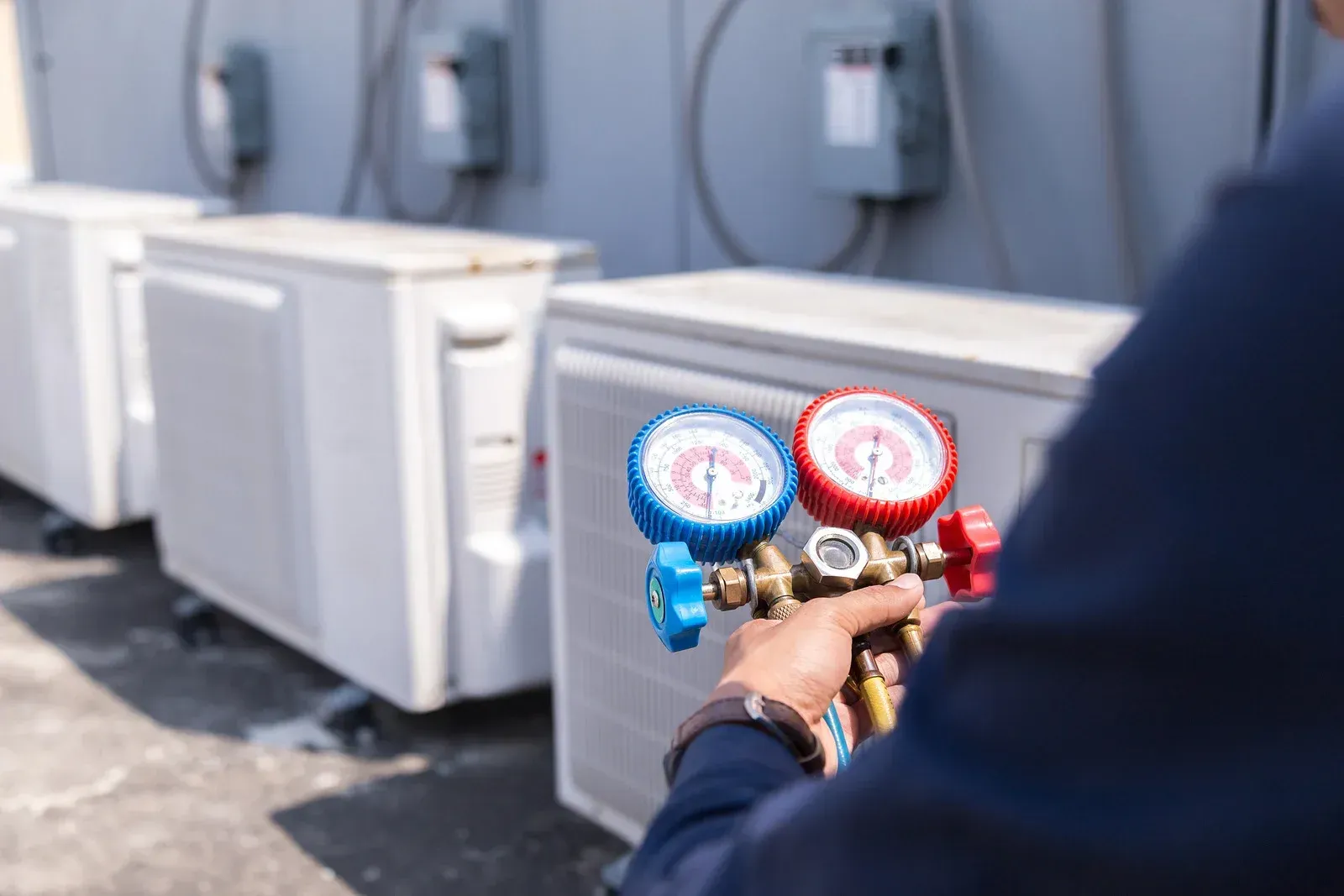 HVAC technician with gauges checking an outdoor air conditioning unit.