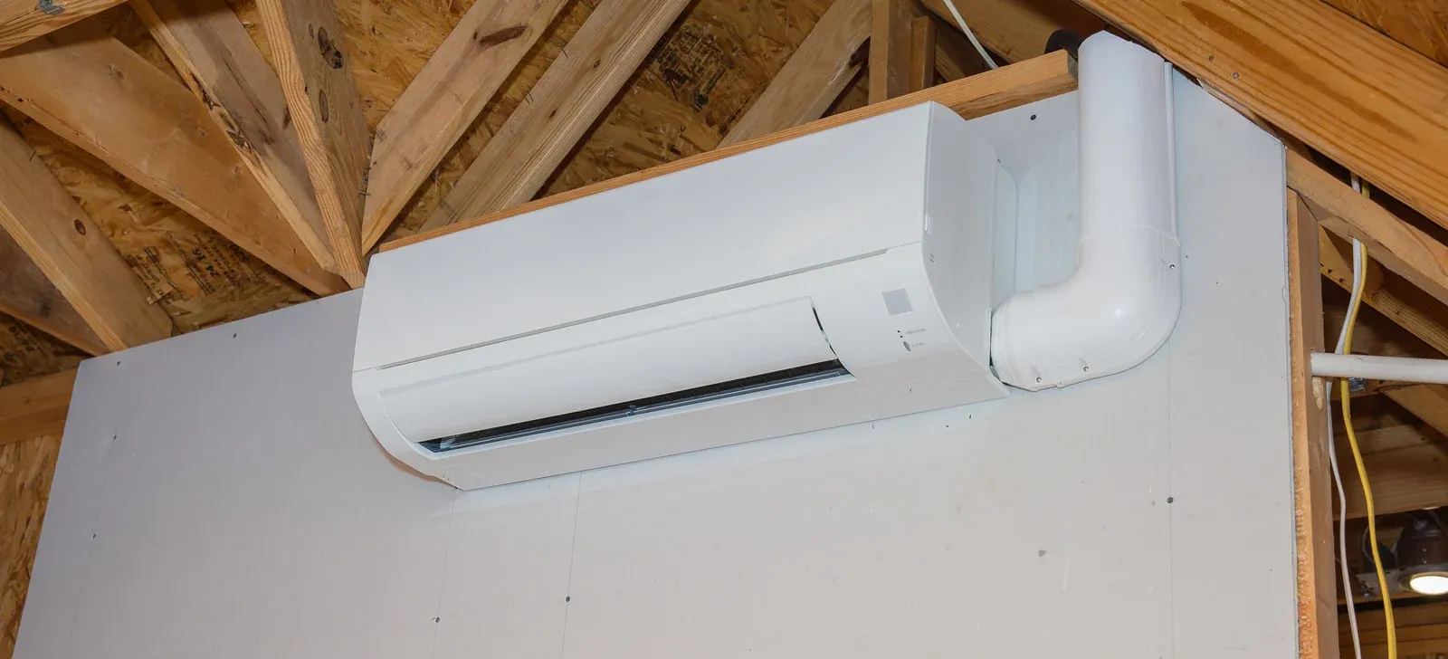 Outdoor air conditioning unit against a beige brick wall, next to a hose and electrical box.