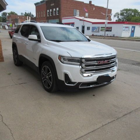 White GMC Acadia SUV parked on a sidewalk in front of buildings on a street.