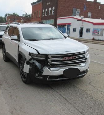 White GMC Acadia SUV with front-end damage on a street, buildings in the background.