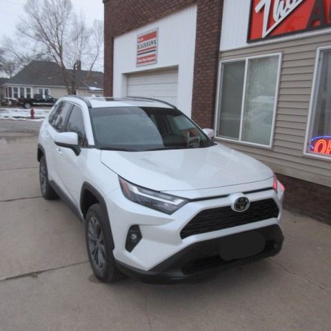 White Toyota RAV4 SUV parked in front of a brick building with a garage door and sign.
