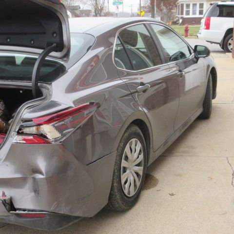 Damaged gray sedan with an open trunk and dented rear. Street scene.
