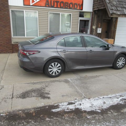 Gray sedan parked on sidewalk in front of an autobody shop.