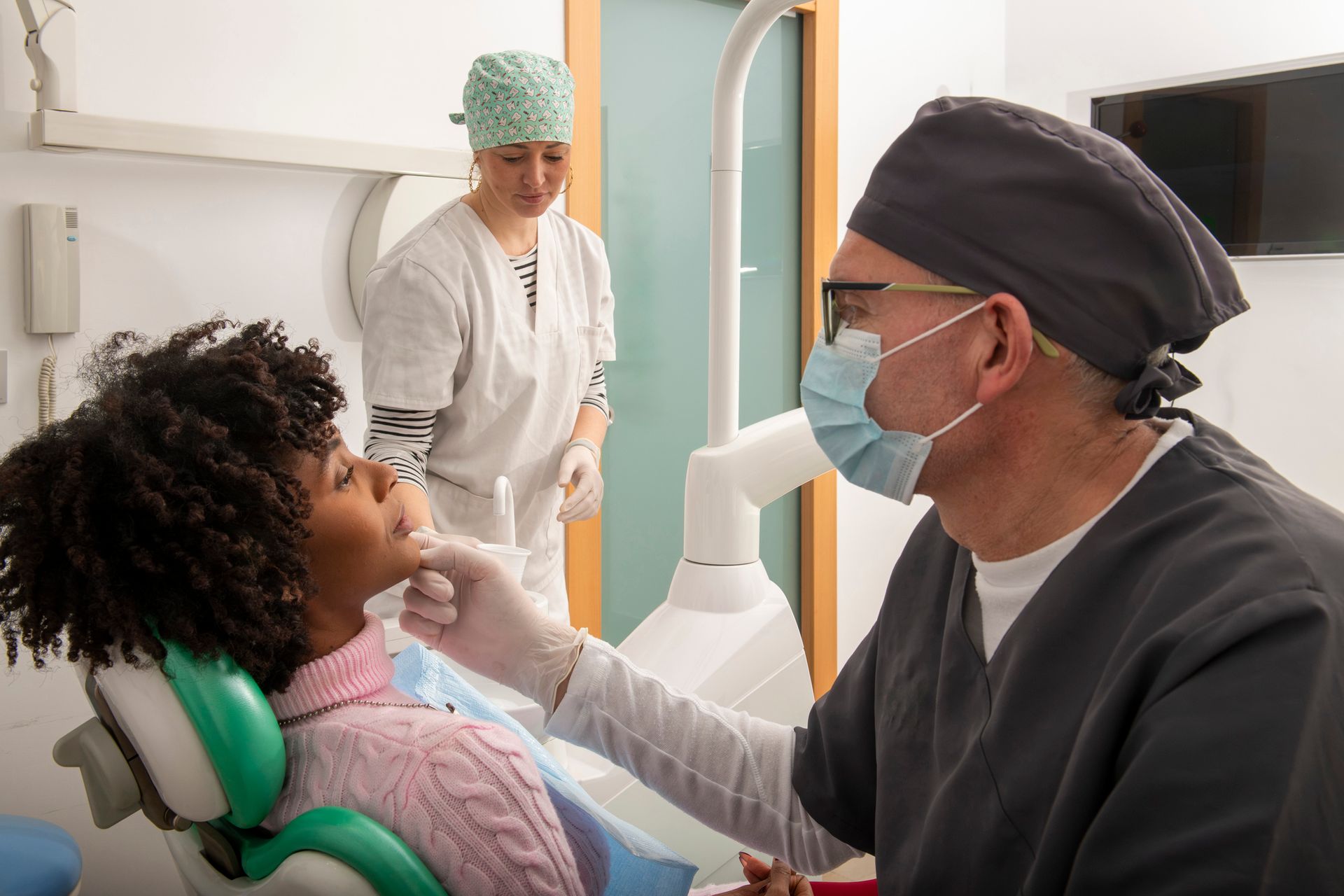 A dentist is examining a patient's teeth while a dental assistant prepares tools.