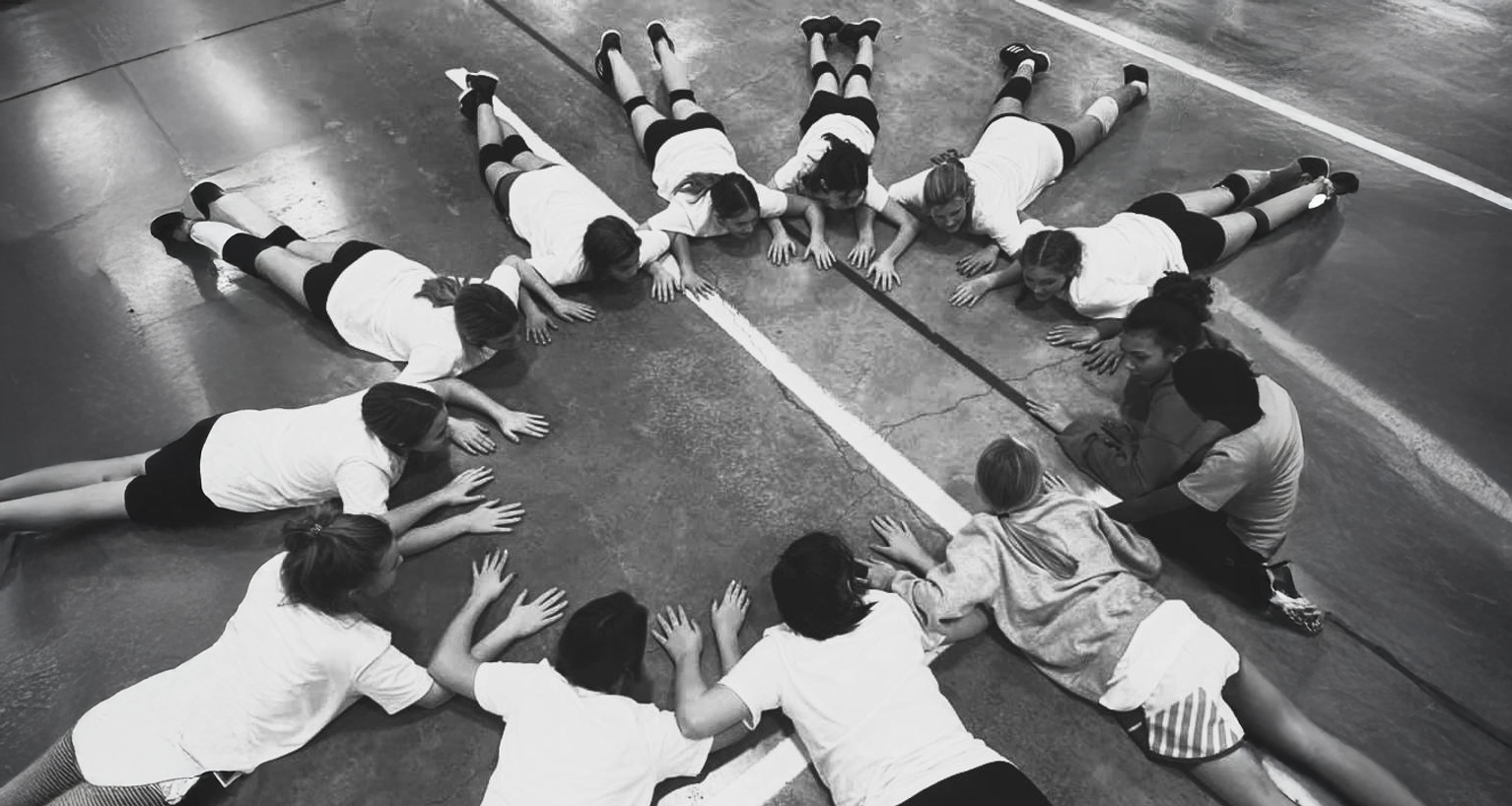 Children in gym class stretching with balls, raising arms.