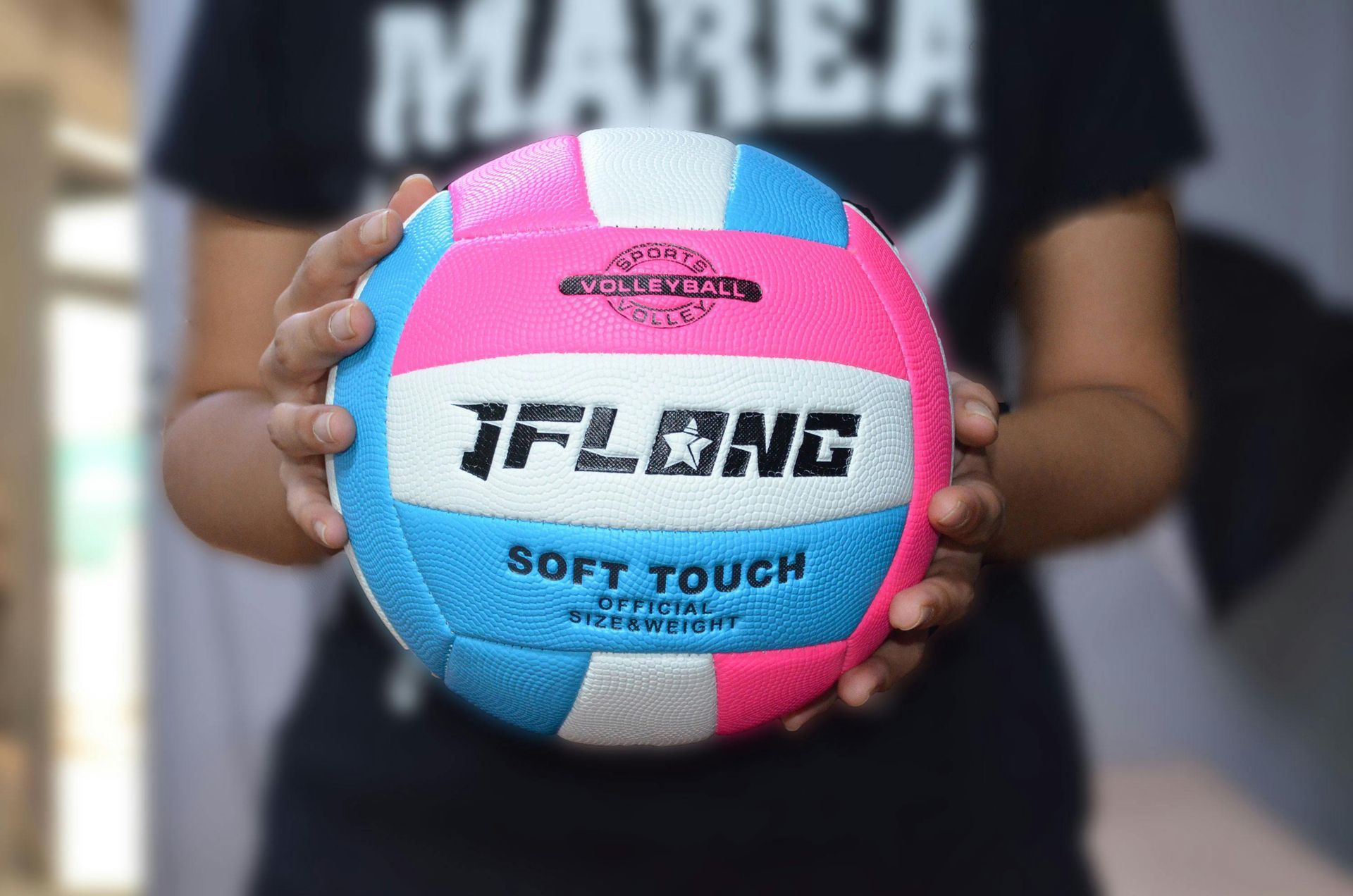 Person holding a multi-colored volleyball, pink, blue, and white, with the text 