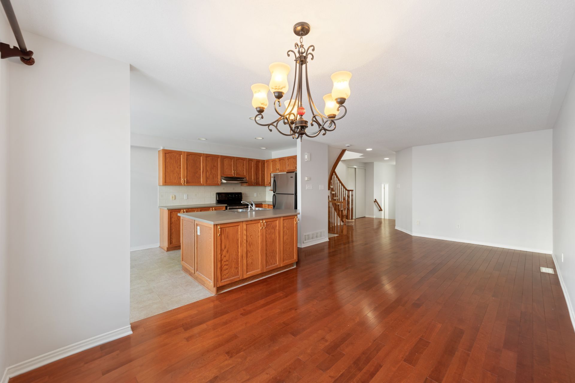 An empty house with hardwood floors and a chandelier hanging from the ceiling.