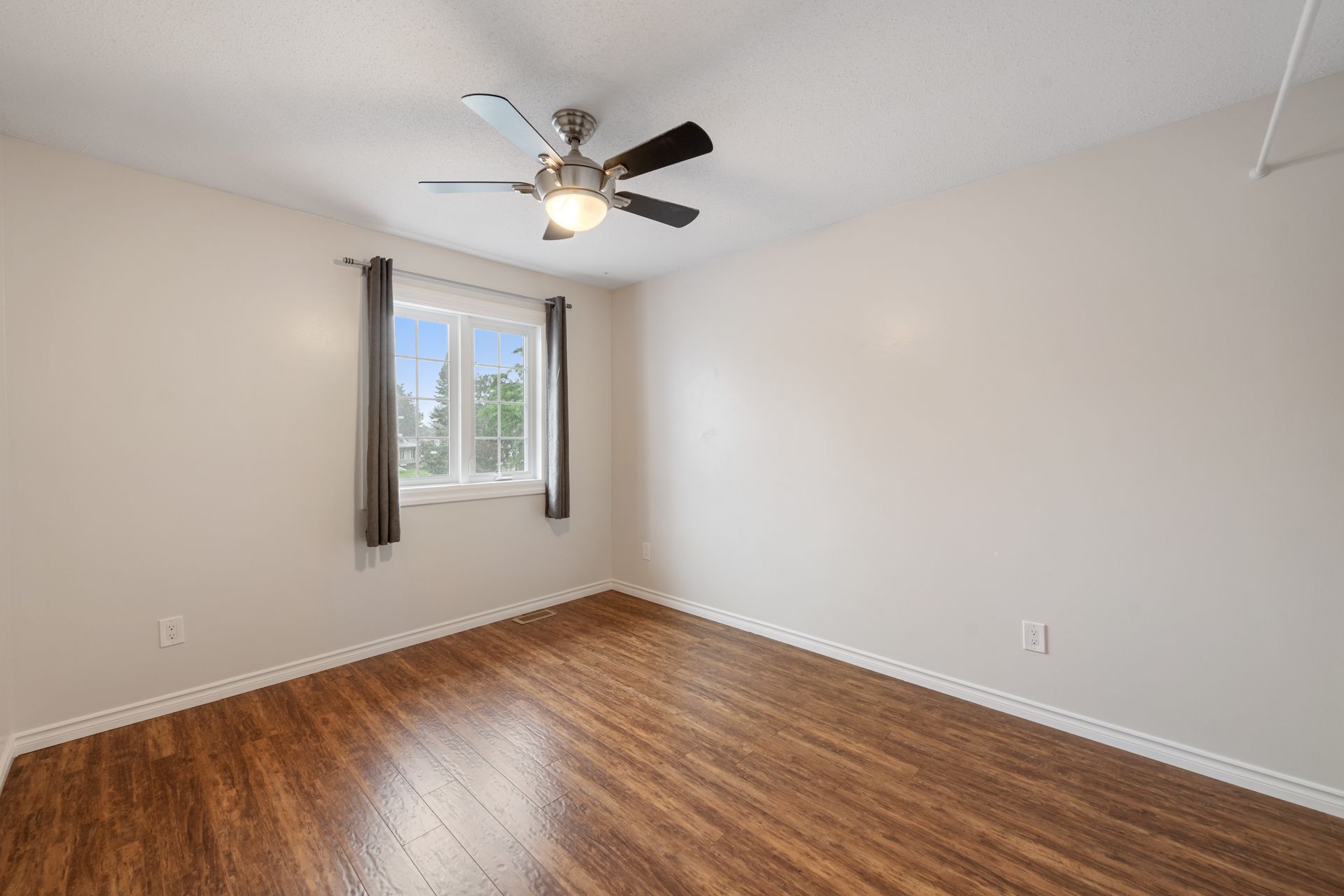 An empty bedroom with hardwood floors and a ceiling fan.