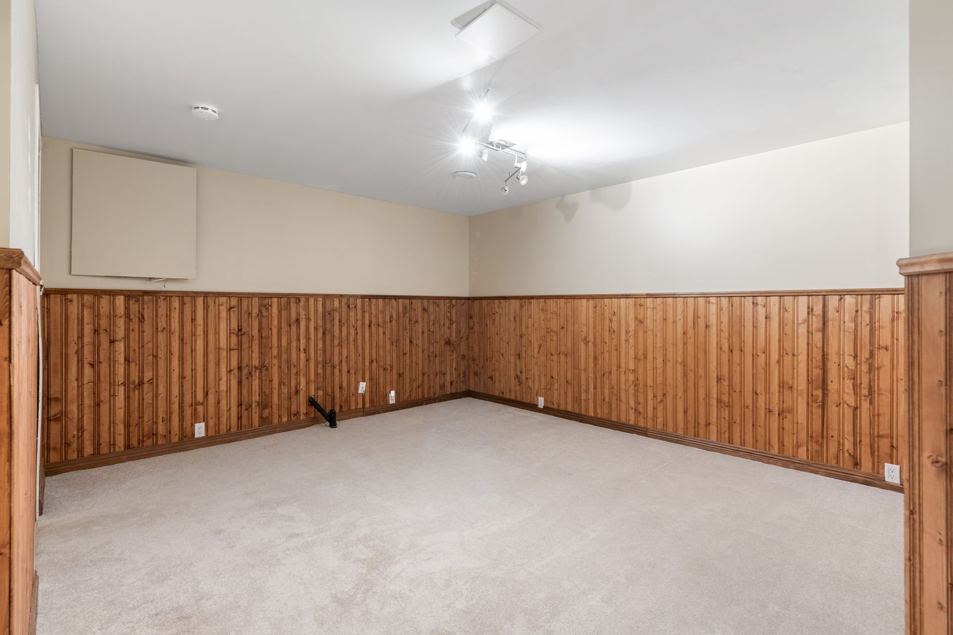 An empty room with wood paneling and a carpeted floor.