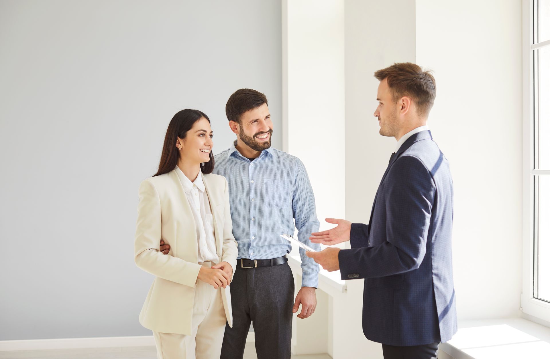 Three professionals talking in a bright office, one gesturing while the others listen with smiles.