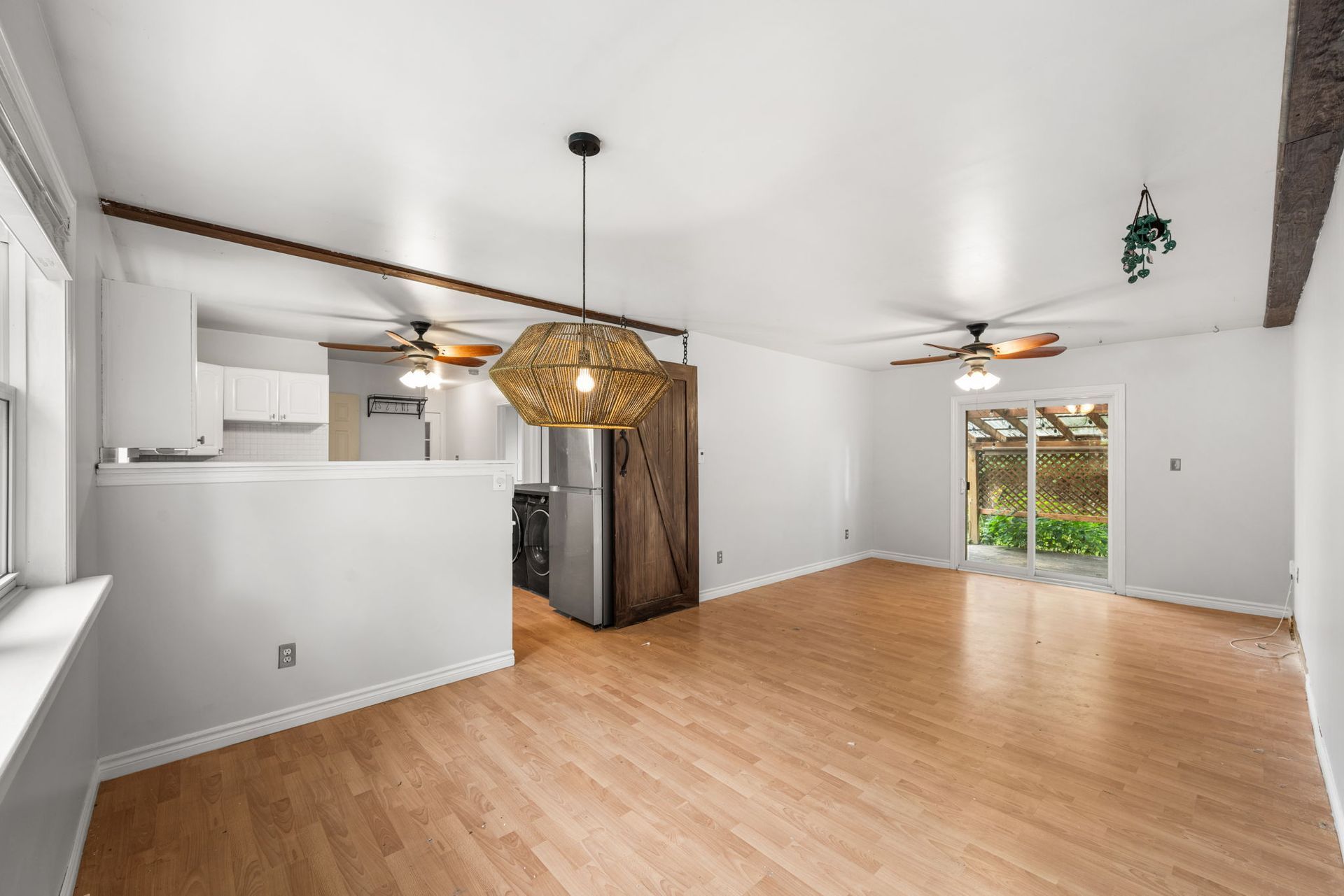 Open-concept living space with light wood floors, white walls, and a large woven pendant light.