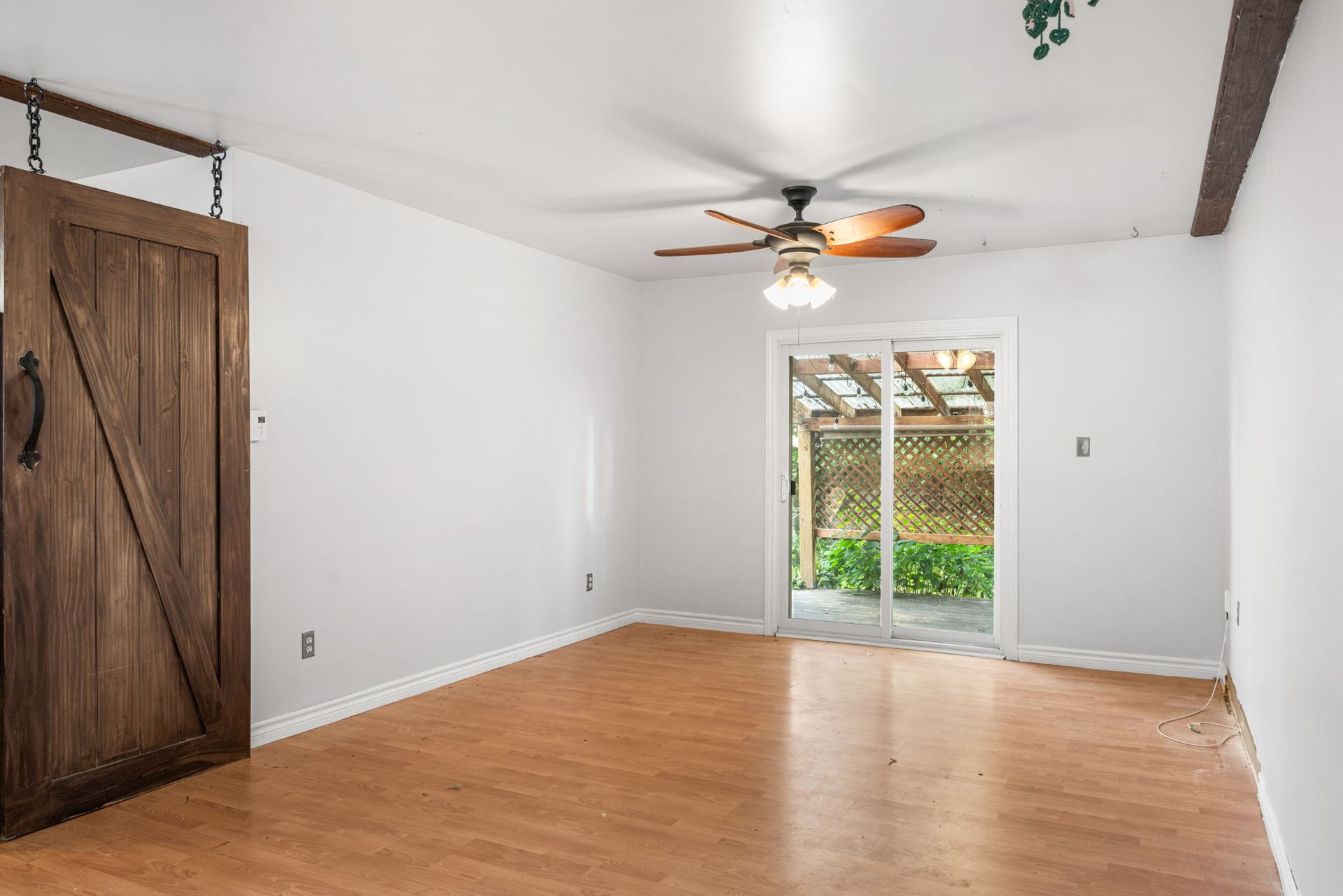 Empty room with wood floors, sliding glass door to a yard, and a wooden barn door.